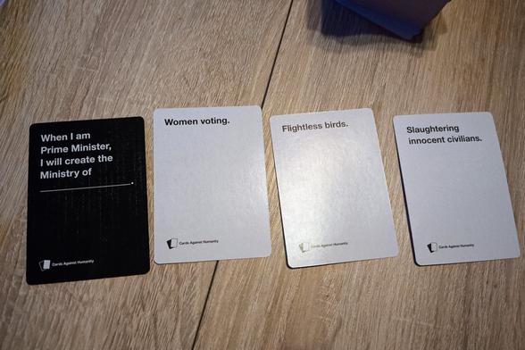 Schwarze Fragekarte: When I am Prime Minister, I will create the Ministry of ____.

Daneben liegen drei weiße Antwortkarte.
1. Women voting.
2. Flightless birds.
3. Slaughtering innocent civilians.